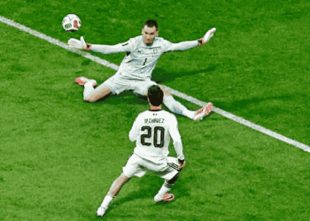 Soccer goalkeeper dives to save the ball as an opposing player wearing number 20, M. Chavez, approaches on a green pitch.