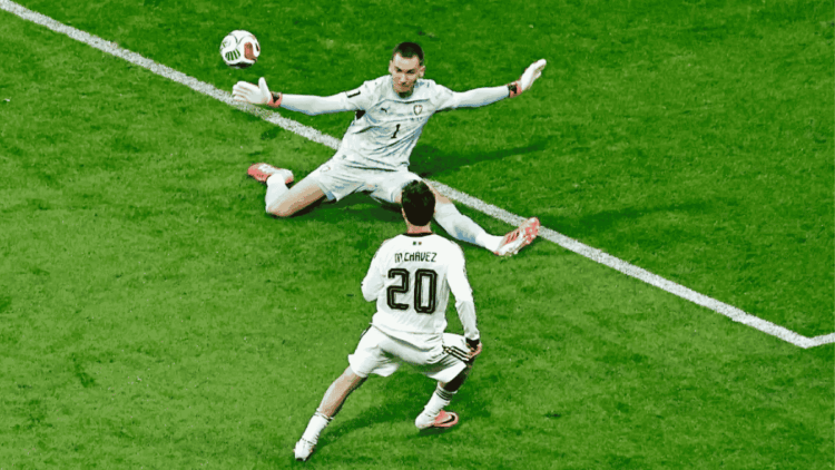 Soccer goalkeeper dives to save the ball as an opposing player wearing number 20, M. Chavez, approaches on a green pitch.